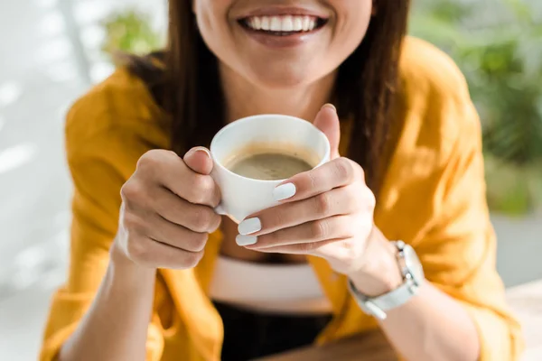 Recortado vista de sonriente freelancer sosteniendo taza de café en casa oficina - foto de stock