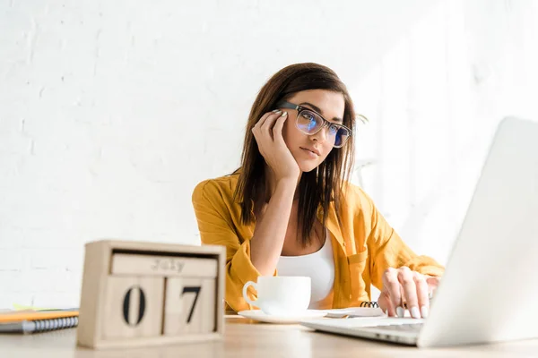 Freelance ennuyé travaillant sur ordinateur portable avec calendrier et café dans le bureau à la maison — Photo de stock