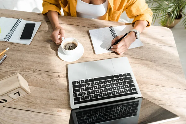 Vista recortada del freelancer que trabaja con el ordenador portátil, portátil y café en la oficina en casa - foto de stock