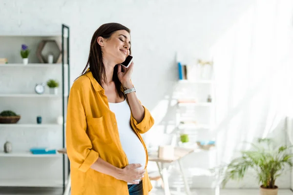 Щасливий вагітний фрілансер у жовтій сорочці, що розмовляє на смартфоні в домашньому офісі — стокове фото