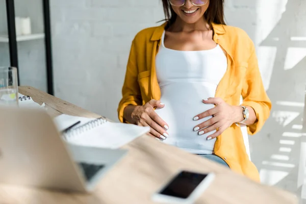 Cropped view of smiling pregnant freelancer sitting in home office — Stock Photo