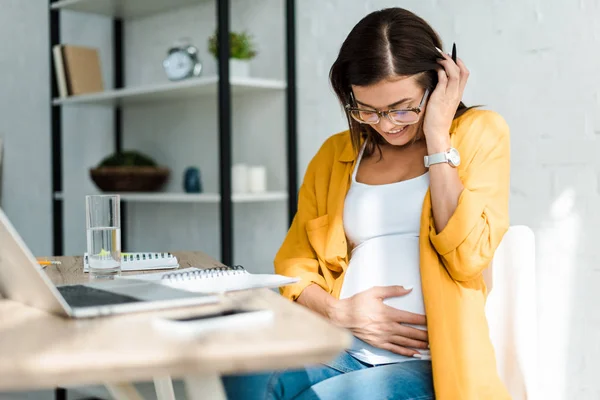 Lächelnde schwangere Freiberuflerin in gelbem Hemd sitzt im Home Office — Stockfoto