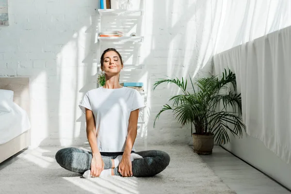 Красива щаслива дівчина з закритими очима практикує йогу в положенні лотоса в спальні вранці — стокове фото