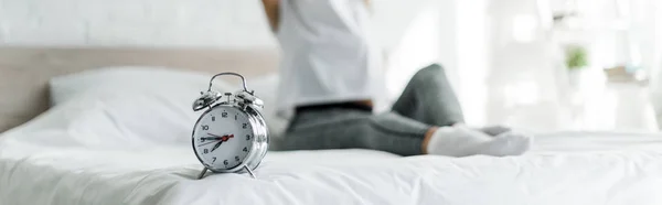 Cropped view of woman sitting with alarm clock on bed — Stock Photo