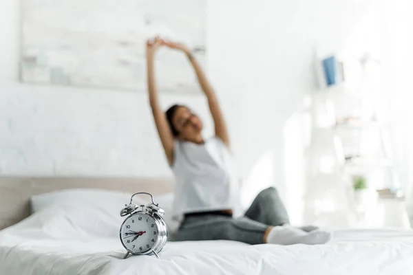 Messa a fuoco selettiva della donna che si estende con sveglia sul letto al mattino — Foto stock