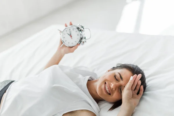 Bela mulher feliz deitado com despertador na cama pela manhã — Fotografia de Stock