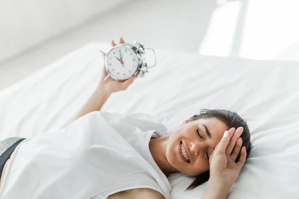 Belle femme heureuse couchée avec réveil sur le lit le matin — Photo de stock