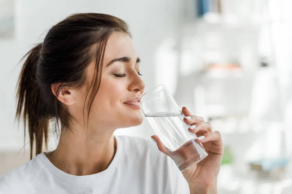 Sonriente chica sosteniendo agua potable de vidrio en la mañana - foto de stock