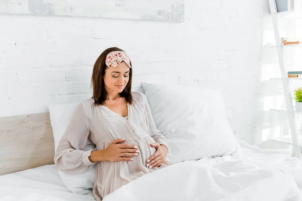 Felice donna incinta in maschera del sonno toccare la pancia mentre sdraiato a letto — Foto stock