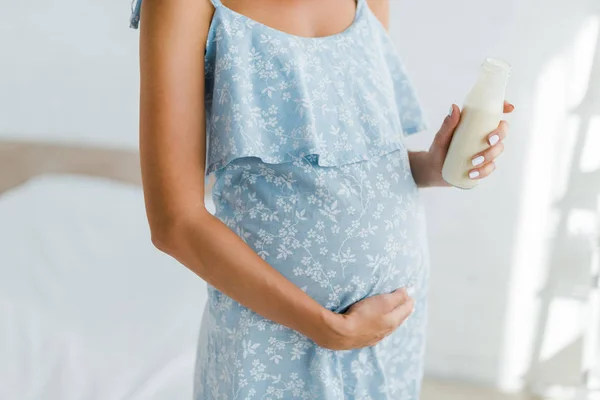 Vista cortada de mulher grávida em vestido azul segurando garrafa de iogurte — Fotografia de Stock