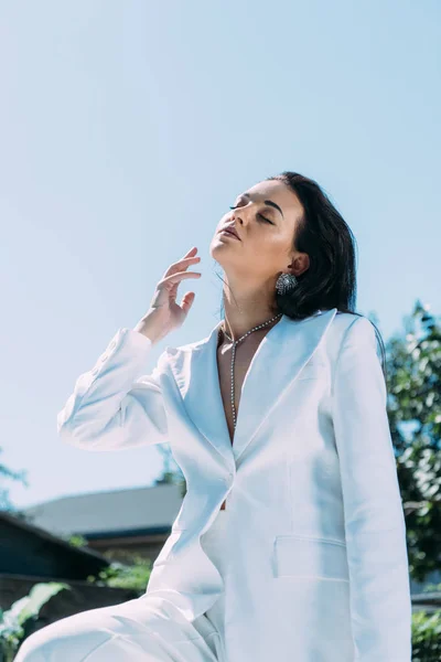 Atractiva mujer en traje blanco posando con los ojos cerrados afuera - foto de stock