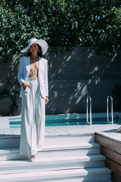 Attraktive Frau in weißem Anzug und Hut posiert und blickt in die Kamera — Stockfoto