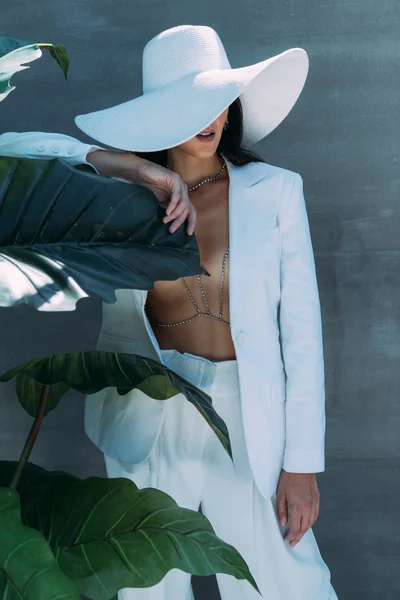 Woman in white suit and hat posing and holding leave outside — Stock Photo