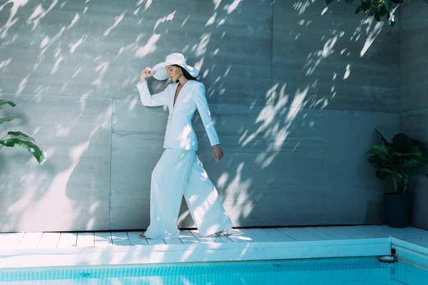 Atractiva mujer en traje blanco y sombrero caminando fuera - foto de stock