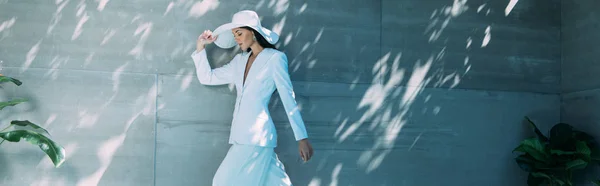 Панорамний знімок привабливої жінки в білому костюмі і капелюсі позує зовні — стокове фото