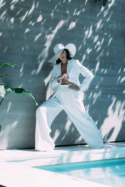 Atractiva mujer en traje blanco y sombrero posando y mirando hacia afuera — Stock Photo