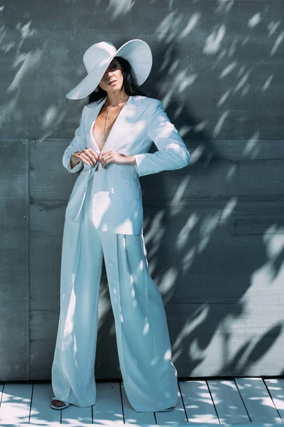 Attrayant femme en costume blanc et chapeau posant et regardant loin à l'extérieur — Photo de stock