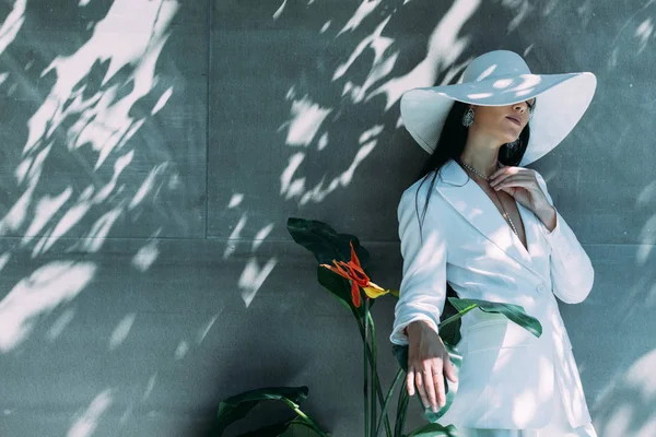 Attraktive Frau in weißem Anzug und Hut posiert mit geschlossenen Augen draußen — Stockfoto