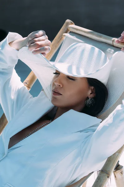 Atractiva mujer en traje blanco y sombrero posando con los ojos cerrados afuera - foto de stock