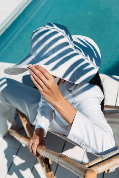Vista de ángulo alto de la mujer en traje blanco y sombrero posando fuera - foto de stock