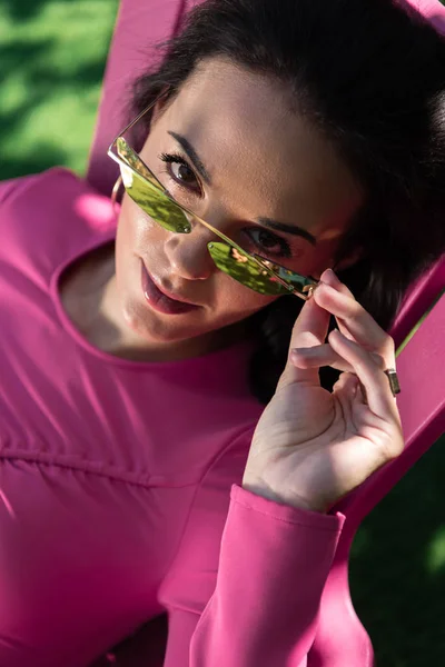 Atractiva mujer en vestido y gafas de sol posando y mirando a la cámara exterior - foto de stock