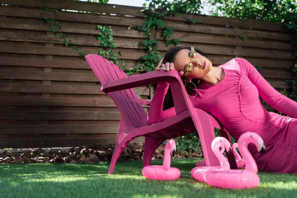 Привлекательная женщина в платье и солнцезащитных очках позирует и сидит на траве снаружи — стоковое фото