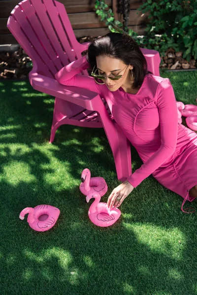 Vista de ángulo alto de la mujer atractiva en vestido y gafas de sol posando y sentado en la hierba exterior - foto de stock