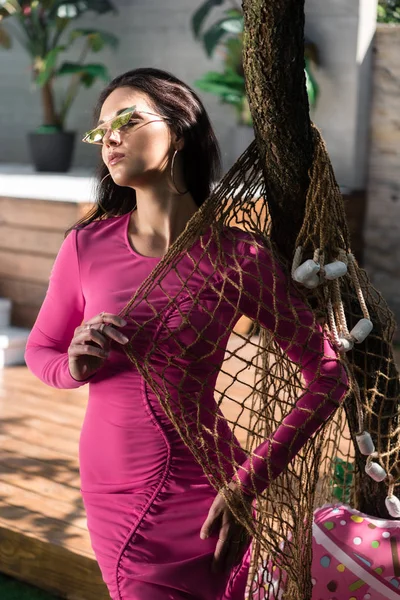 Jolie femme en robe et lunettes de soleil posant les yeux fermés à l'extérieur — Photo de stock