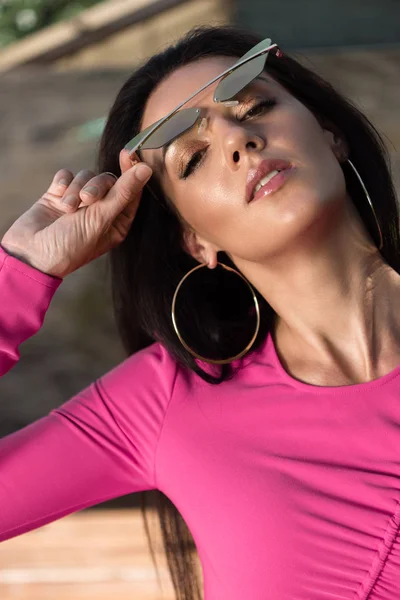 Atractiva mujer en vestido y gafas de sol posando y mirando a la cámara exterior - foto de stock