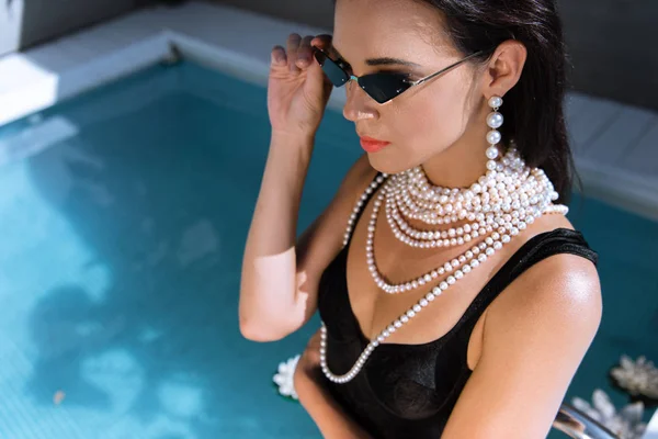 Mulher atraente em maiô preto e óculos de sol posando perto da piscina — Fotografia de Stock