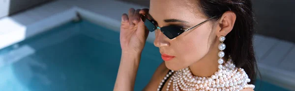 Plano panorámico de mujer atractiva en gafas de sol posando cerca de la piscina - foto de stock