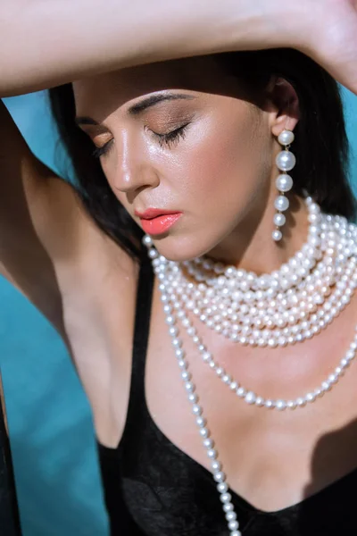 Séduisante femme en maillot de bain noir et collier de perles posant les yeux fermés — Photo de stock