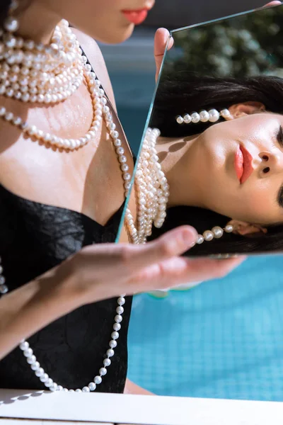 Attractive woman in black swimsuit and pearl necklace looking at mirror — Stock Photo