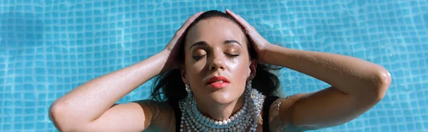 Panoramic shot of attractive woman in pearl necklace posing in pool — Stock Photo