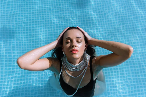 Vista superior de mujer atractiva en traje de baño negro y collar de perlas posando en la piscina - foto de stock