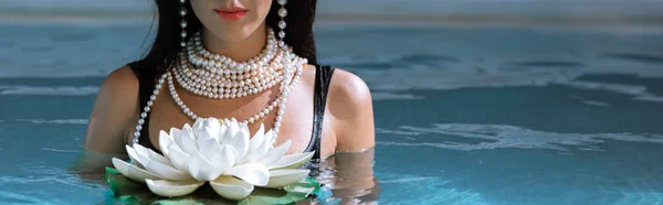 Panoramic shot of woman in black swimsuit and pearl necklace posing in pool — Stock Photo