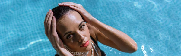 Panoramic shot of attractive woman in pearl necklace posing in pool — Stock Photo