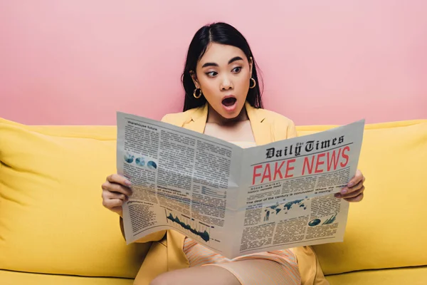 Sorprendido asiático mujer holding periódico con falso noticias aislado en rosa — Stock Photo