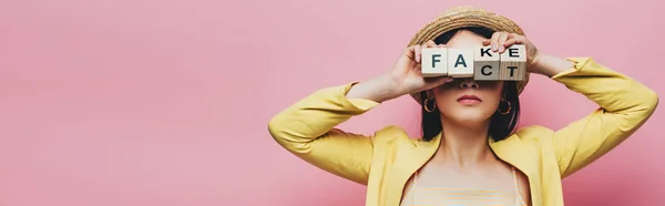 Tiro panorâmico de mulher asiática segurando cubos de madeira na frente da cara com falso e fato lettering isolado no rosa — Fotografia de Stock