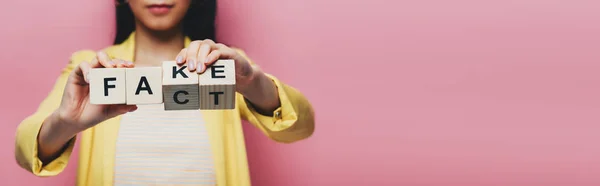 Vista recortada de mujer asiática sosteniendo cubos de madera con letras falsas y hechos aislados en rosa, tiro panorámico - foto de stock