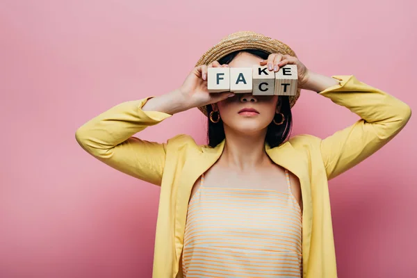 Asiática mulher segurando cubos de madeira na frente da cara com falso e fato lettering isolado no rosa — Fotografia de Stock