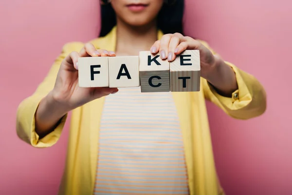 Cropped view of asian woman holding wooden cubes with fake and fact lettering isolated on pink — Stock Photo