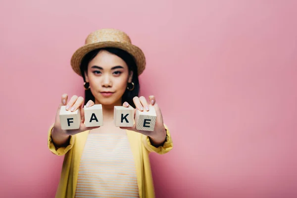 Foco seletivo de mulher asiática segurando cubos de madeira com letras falsas e fatos isolados em rosa — Fotografia de Stock