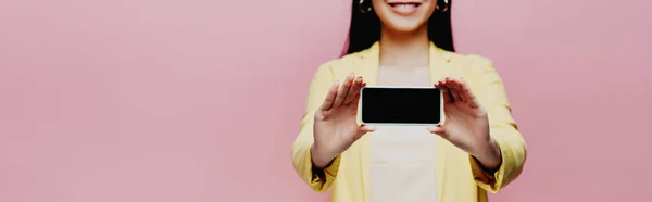 Corte vista de feliz asiático mulher no amarelo roupa segurando smartphone com tela em branco isolado no rosa, panorâmica tiro — Fotografia de Stock