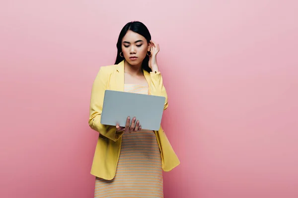Азиатка в желтом наряде держит ноутбук изолирован на розовый — стоковое фото