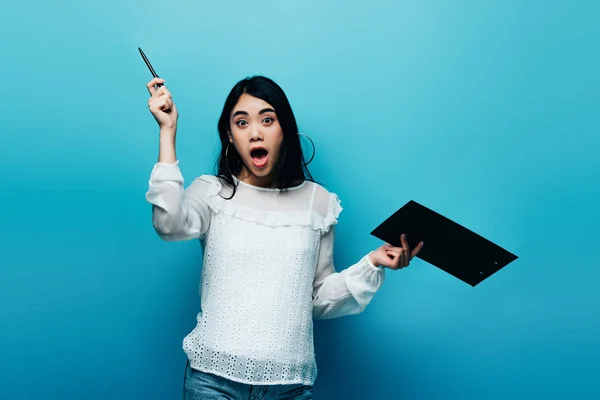 Animado asiático jornalista no branco blusa segurando prancheta no azul fundo — Fotografia de Stock