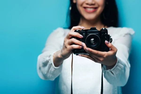 Recortado vista de sonriente asiático mujer en blanco blusa celebración digital cámara en azul fondo - foto de stock