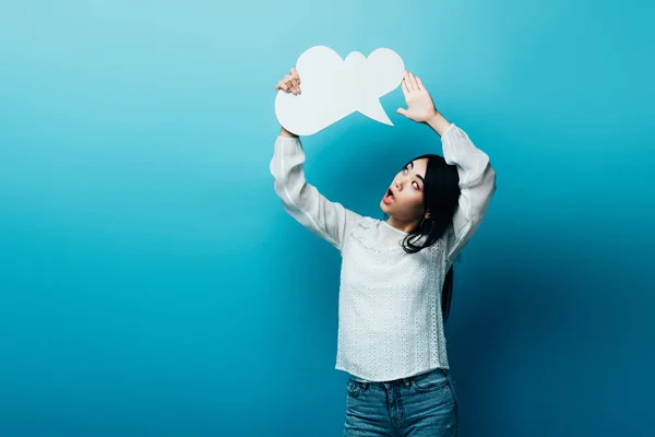Shocked brunette asian woman holding blank thought bubble on blue background — Stock Photo
