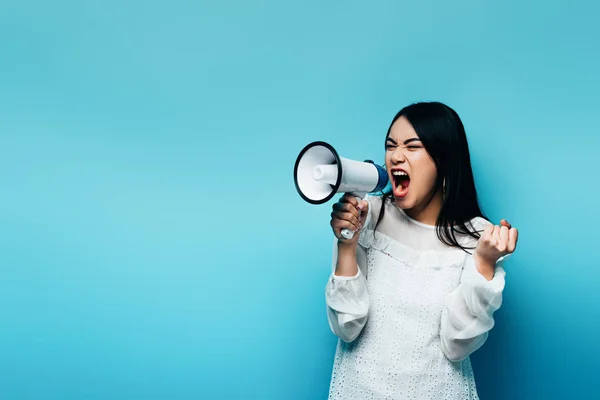 En colère brunette asiatique femme crier dans haut-parleur sur fond bleu — Photo de stock