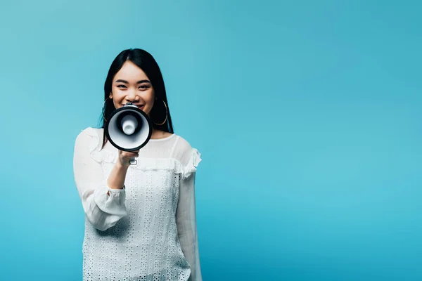 Sonriente morena asiática mujer sosteniendo altavoz sobre fondo azul - foto de stock